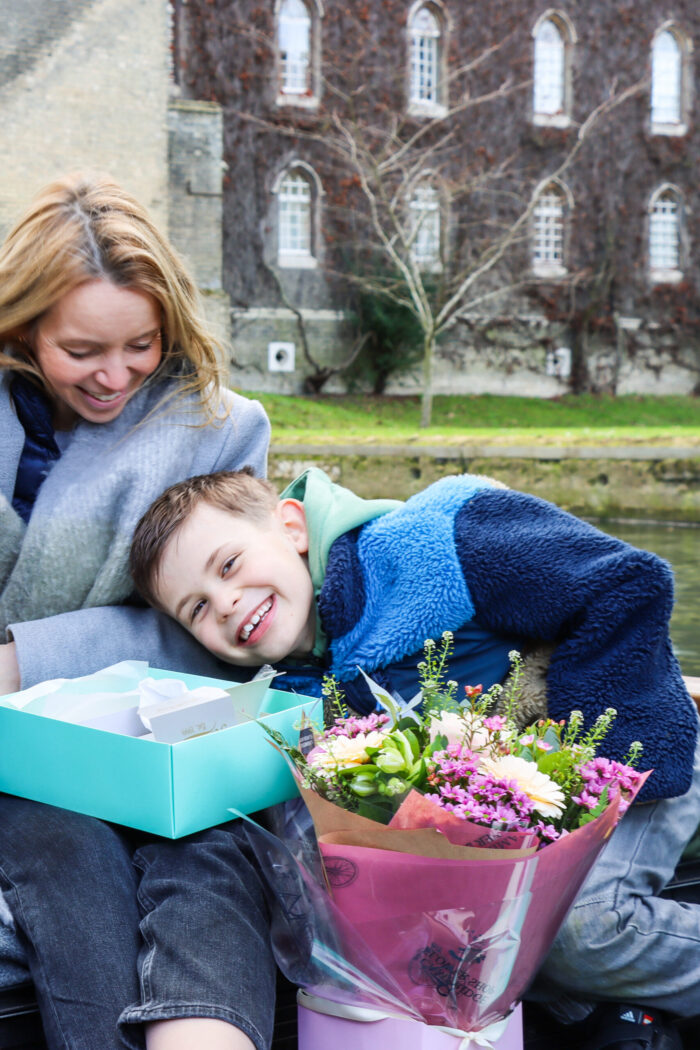 mother and son on a chauffeured punt with a seasonal bouquet of flowers and picnic box in front of the virginia creeper at St Johns College Cambridge