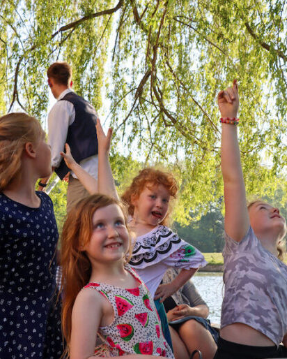 children reaching up to grab the branches as they are punted under the tress on the river Cam in Cambridge.